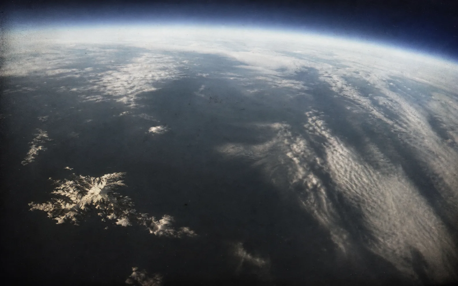 A grainy aerial plate shows Iceland at the edge of the North Atlantic beneath a curved horizon.